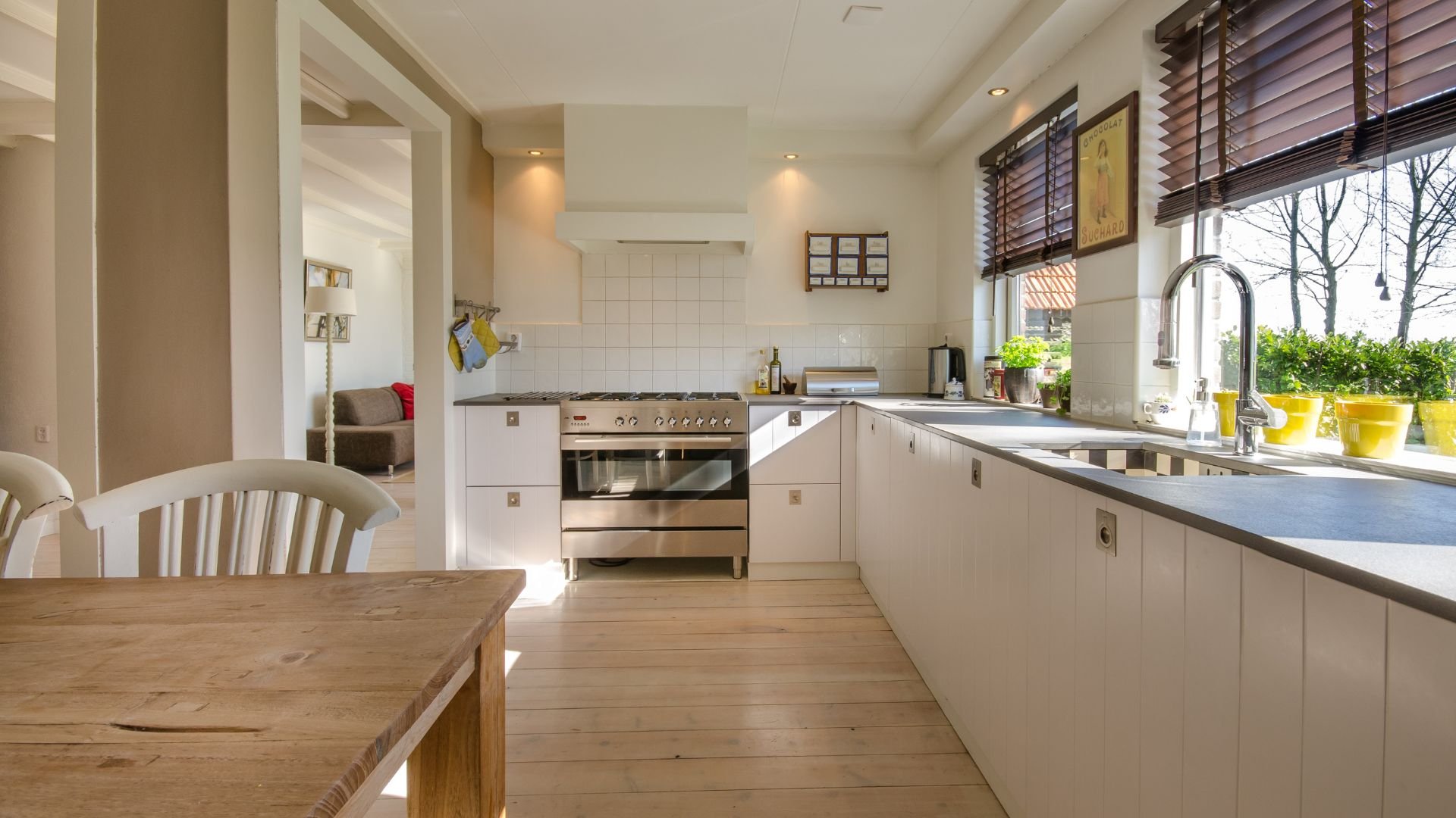 Modern white kitchen with wooden table, stainless steel appliances, and window