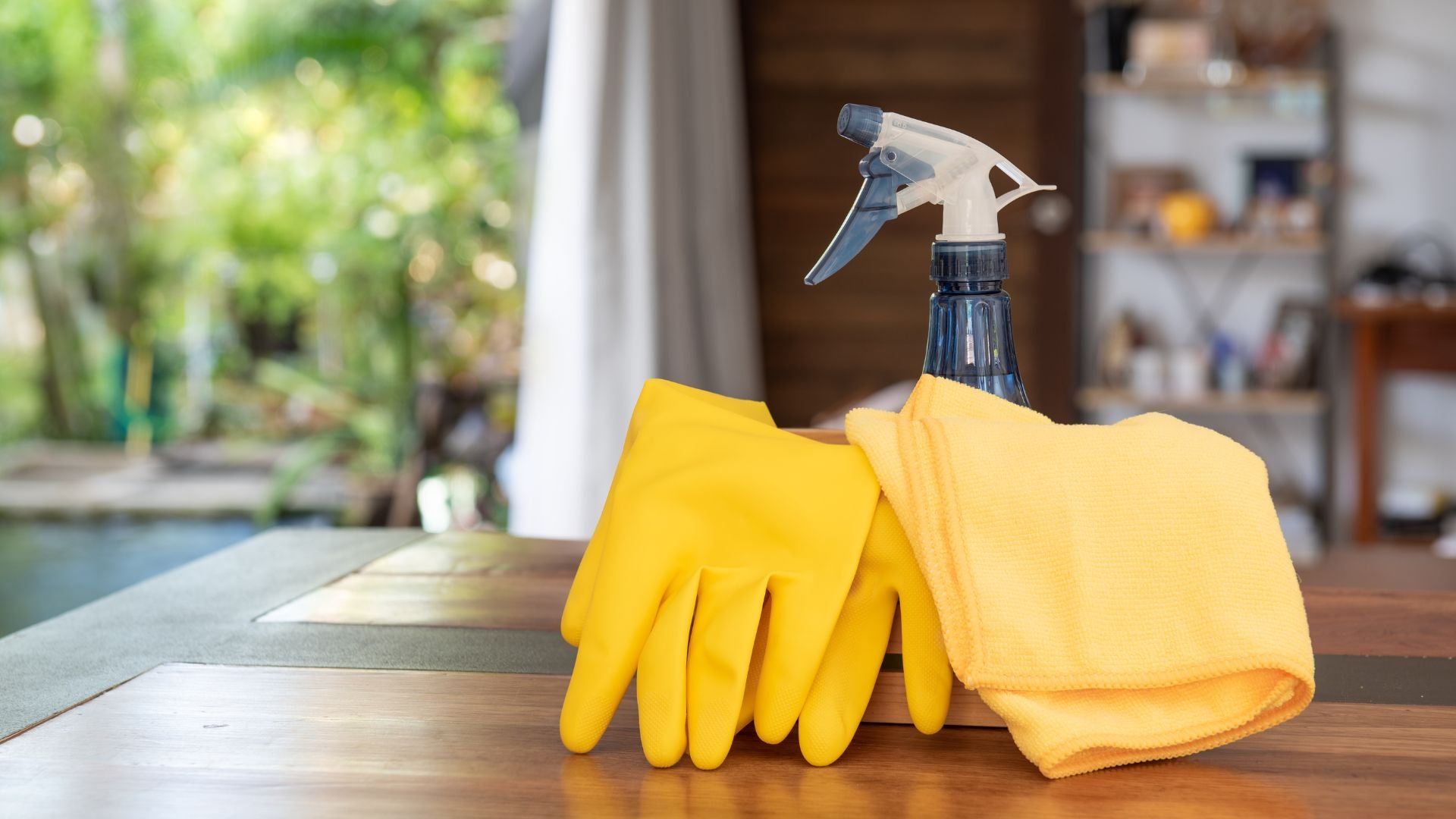 Yellow cleaning gloves, spray bottle, and cloth on wooden surface