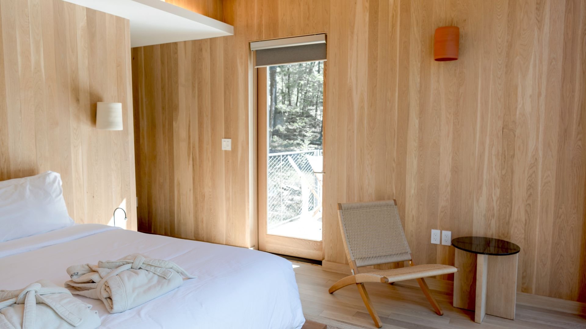 Minimalist wooden bedroom with white bed and forest view through window
